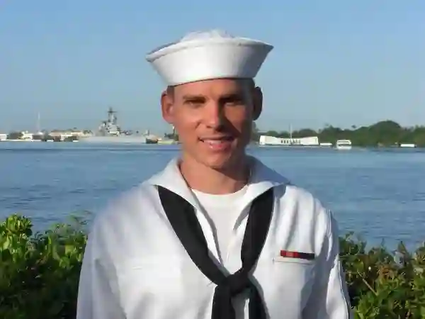 A United States Navy Sailor at the Pearl Harbor National Memorial with the USS Arizona Memorial and USS Missouri in the Background